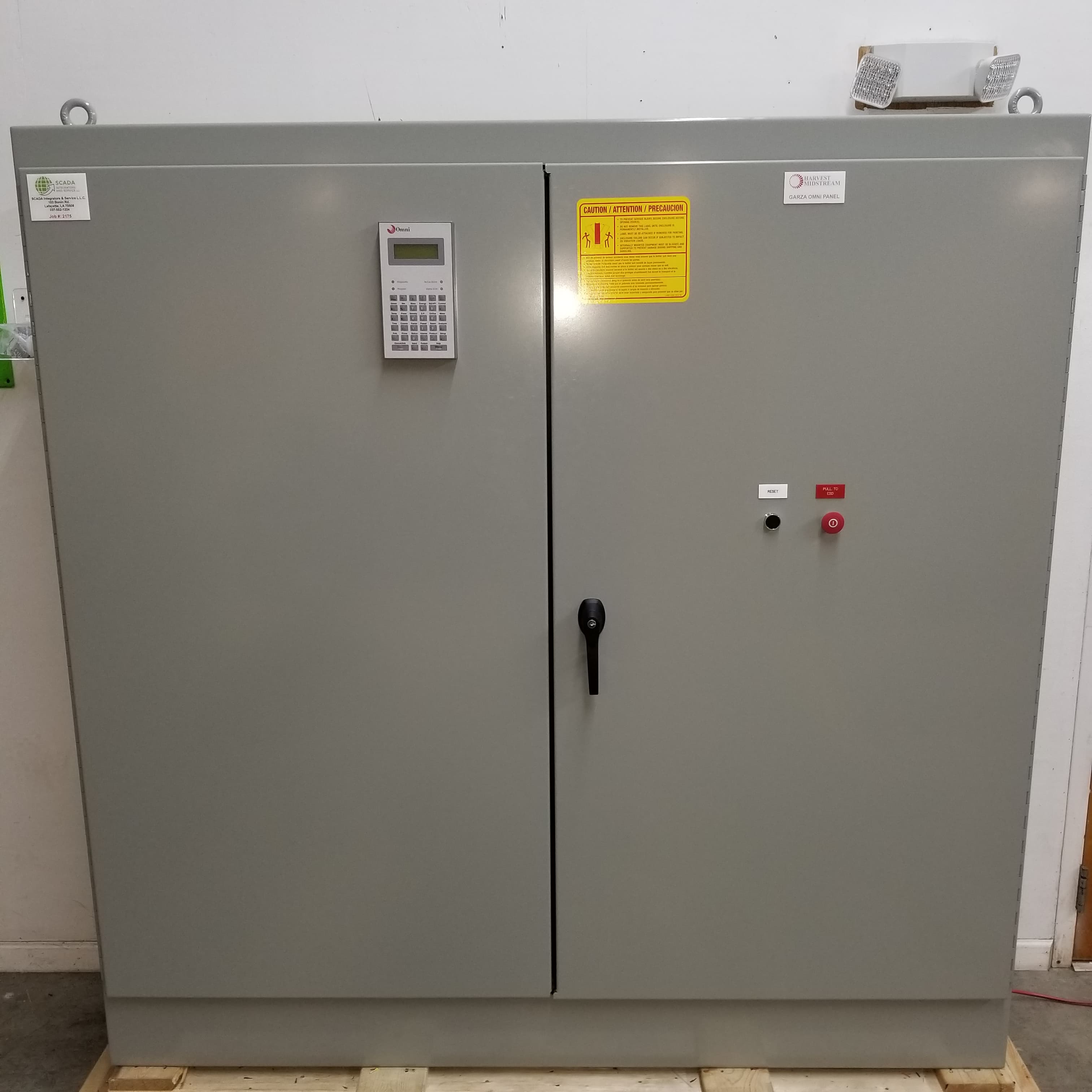 Grey industrial control cabinet with digital keypad, warning label, and red emergency stop button.