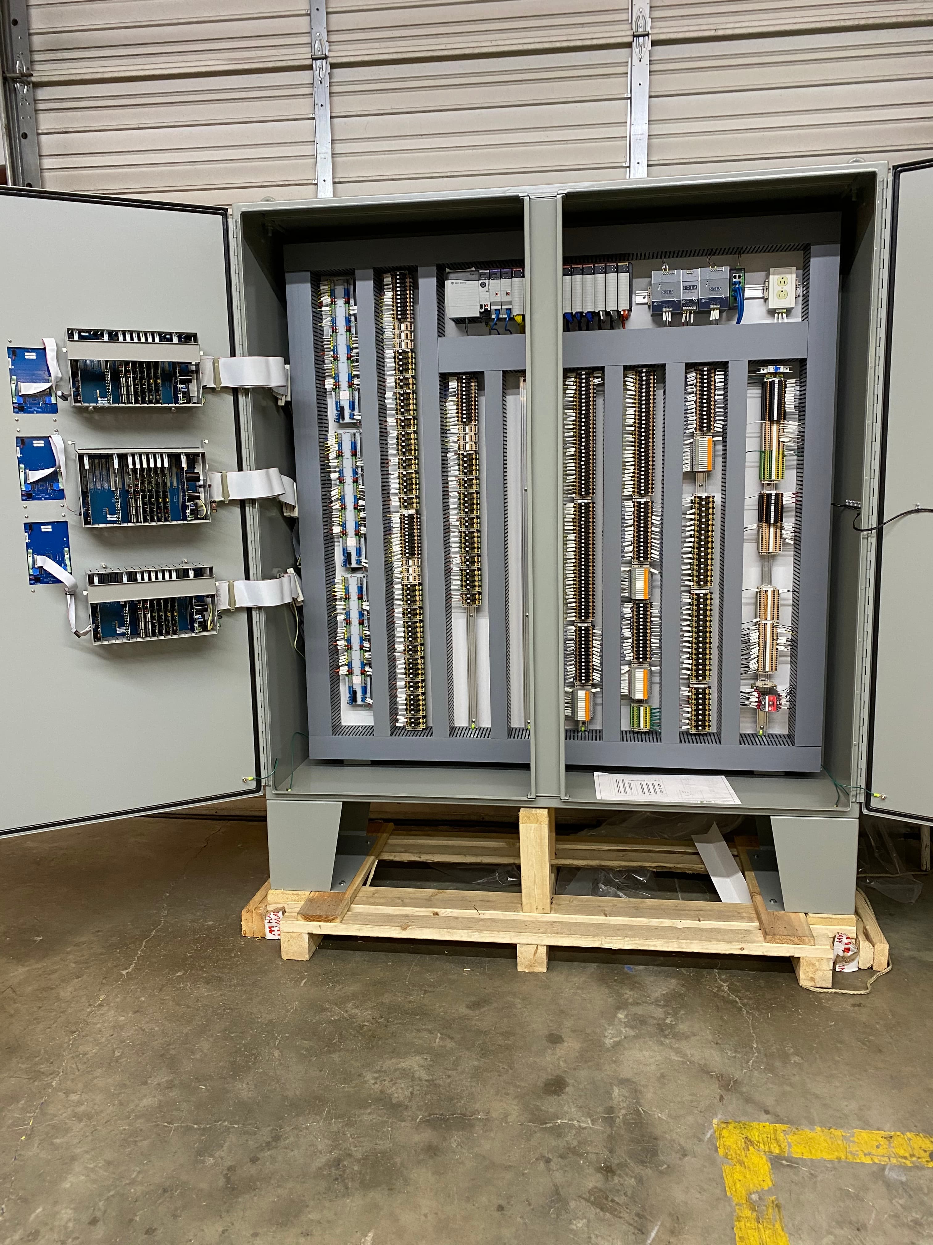 Open industrial electrical control panel with complex wiring and components on a wooden pallet.