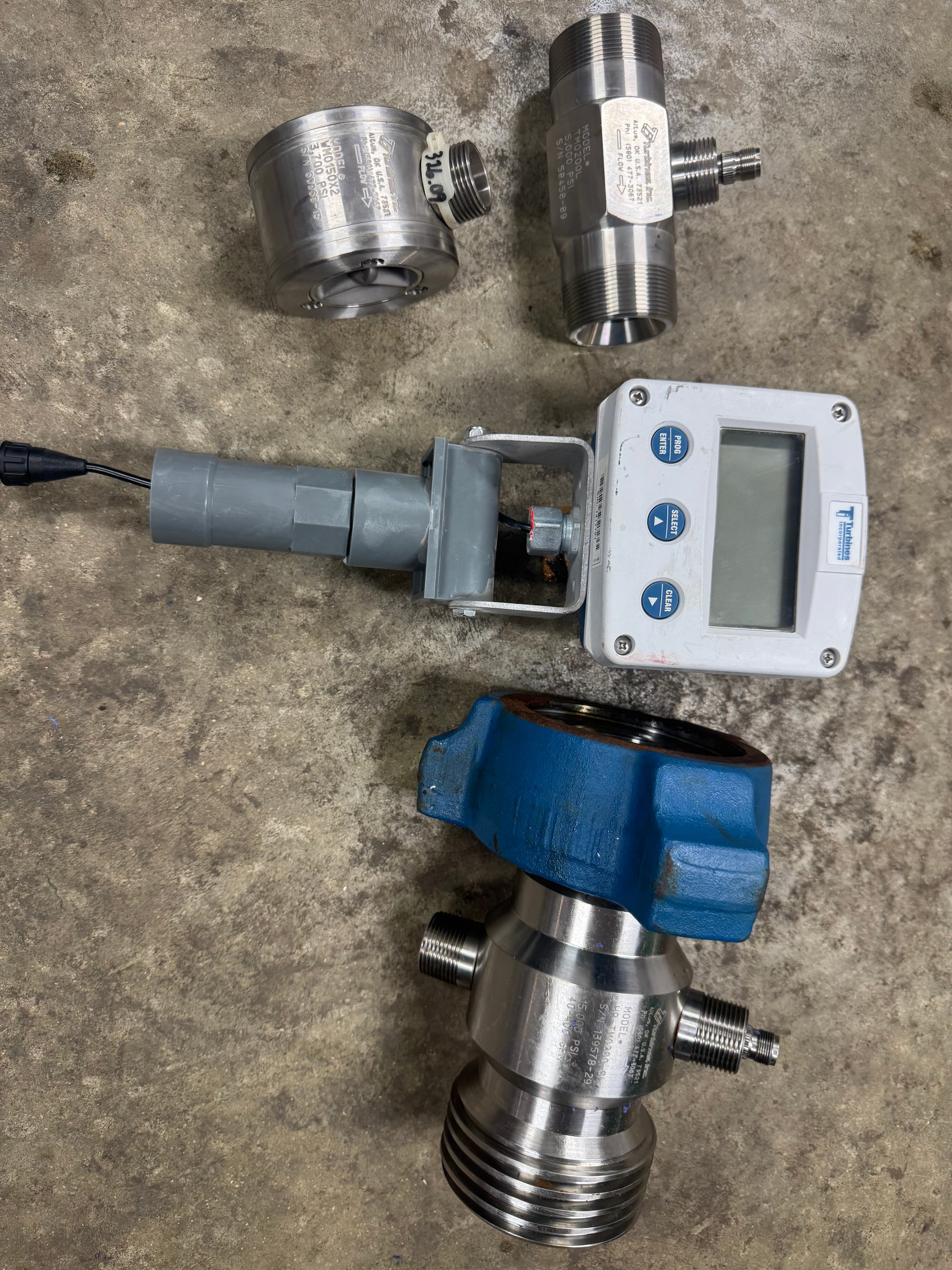 Industrial stainless steel flow meters and a digital display unit on a concrete floor.